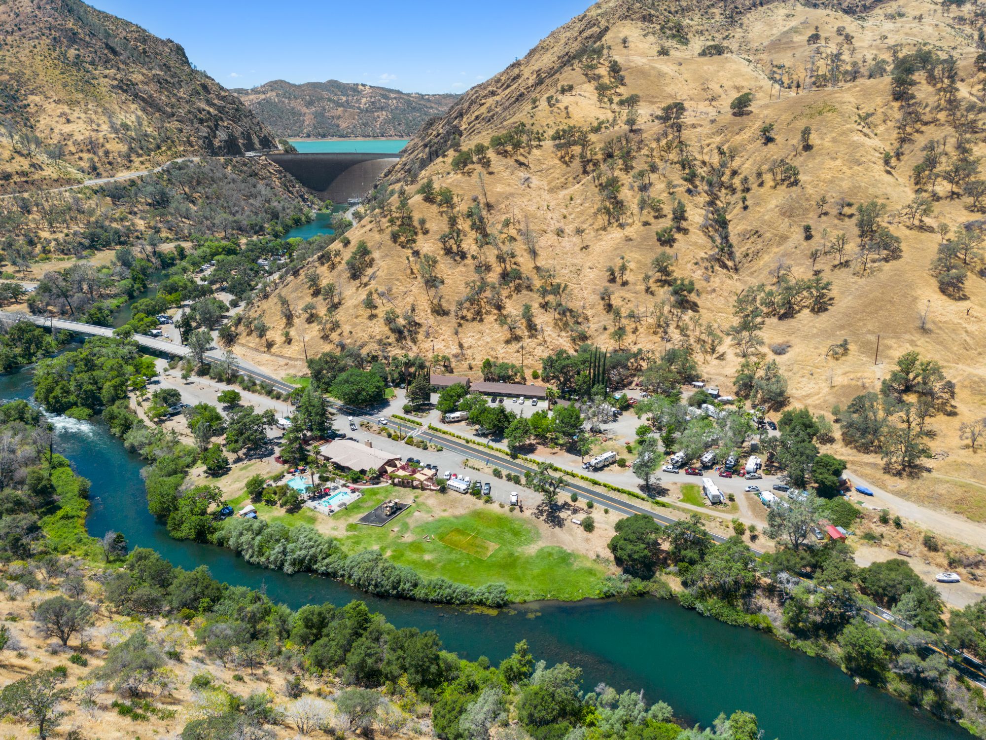 A winding river cuts through a mountainous landscape with a parallel road, surrounded by greenery and scattered buildings.