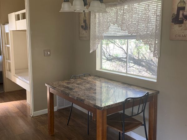 A small dining nook with a marble-top table, two metal chairs, a window with blinds, and a hanging light fixture above the table, in a compact kitchen area.