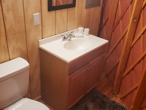 A bathroom with wood-paneled walls, a toilet, a vanity with a sink, mirror, and a gray mat on a wooden floor ends the look.