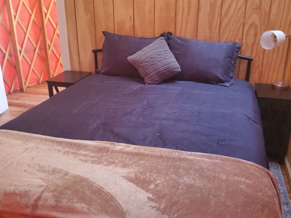 A cozy bedroom with a wooden wall, a neatly made bed with blue bedding, and a small lamp on the bedside table, creating a warm atmosphere.