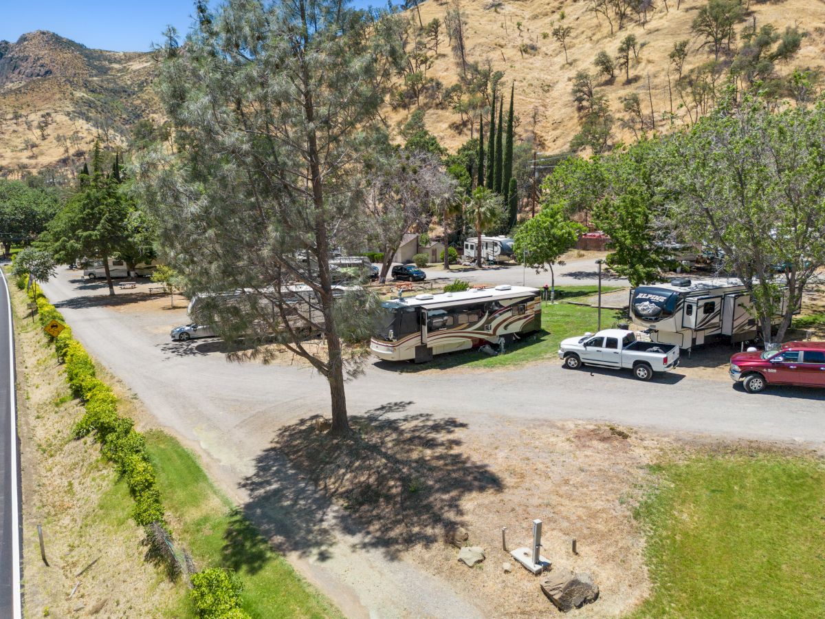 The image shows a campground with RVs and parked vehicles surrounded by trees and hills under a clear sky.