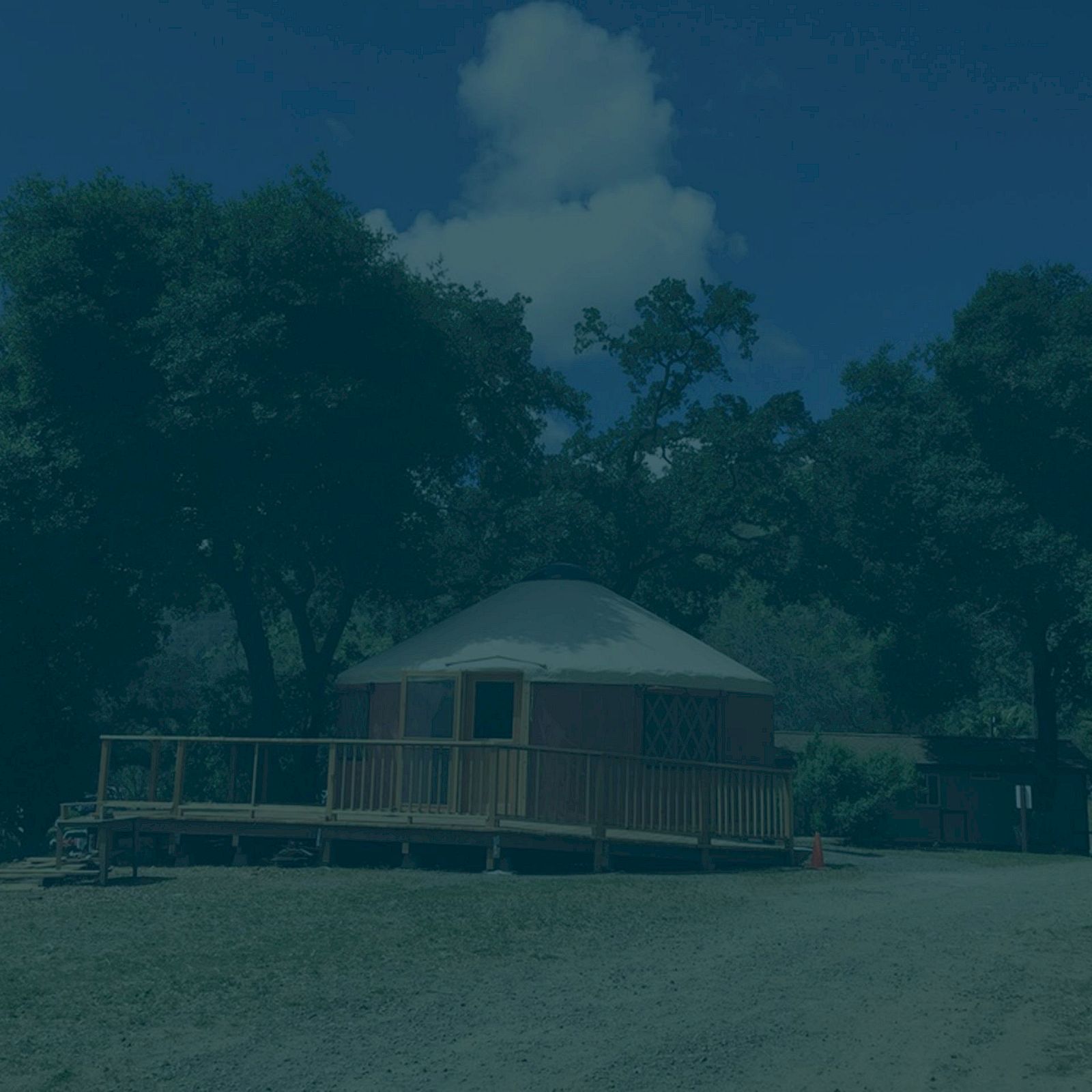 The image shows a yurt with a wooden deck, surrounded by trees under a blue sky with clouds.