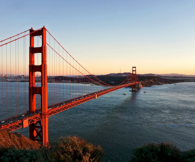 The image shows the Golden Gate Bridge spanning across the water during sunset, with the cityscape and hills in the background.