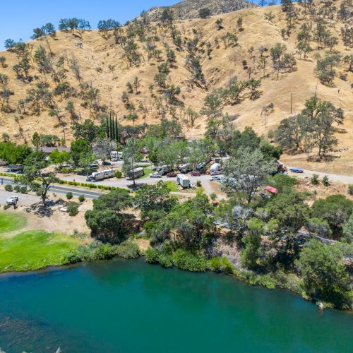 A scenic landscape with a winding river, green vegetation, and rolling hills in the background under a clear blue sky.