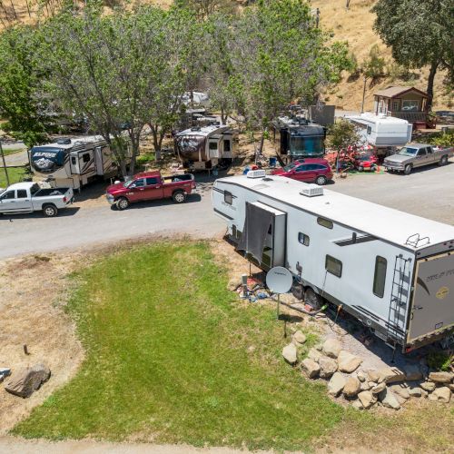 The image shows a group of RVs and vehicles parked in a scenic area with trees and grass, suggesting a camping site.