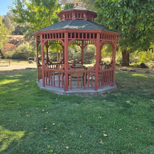 The image shows a wooden gazebo on a grassy area surrounded by trees, capturing a peaceful outdoor setting.